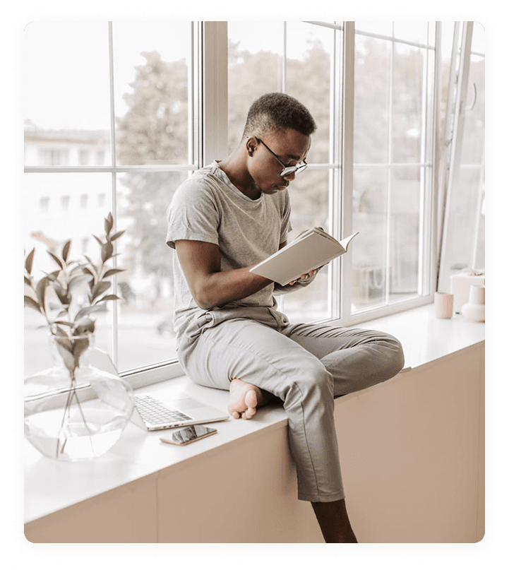 شخص يجلس بجانب نافذة يقرأ كتاباً